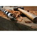 Wooden mallet and metal auger on a wooden surface with wood shavings.